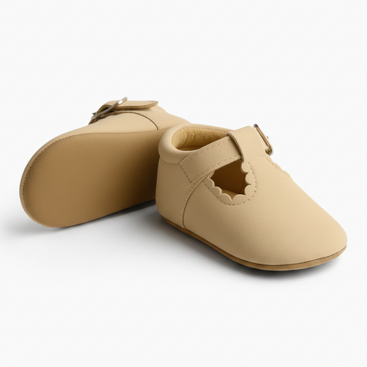 Bébé en train d'apprendre à se tenir debout, les mocassins beiges offrant une semelle antidérapante essentielle.