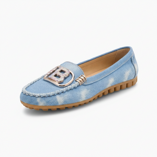 Mocassins en jean bleu pour femme, ornés de bijoux élégants, portés avec style sur un trottoir urbain.