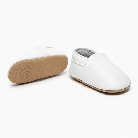 Pied de bébé chaussé d'un mocassin en cuir blanc, offrant confort et maintien sécurisé.