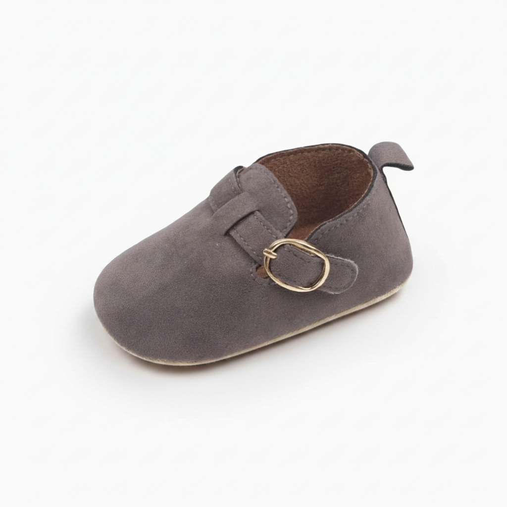 Mocassin bébé gris en daim, idéal pour les premiers pas, délicatement posé sur un plancher en bois clair.