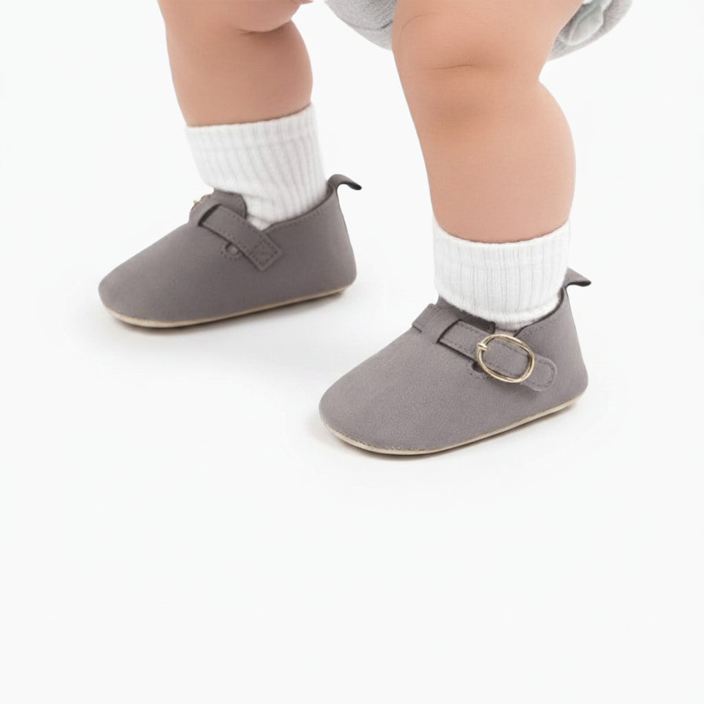 Pieds de bébé confortablement chaussés des mocassins gris en daim, vus de face sur un tapis douillet.