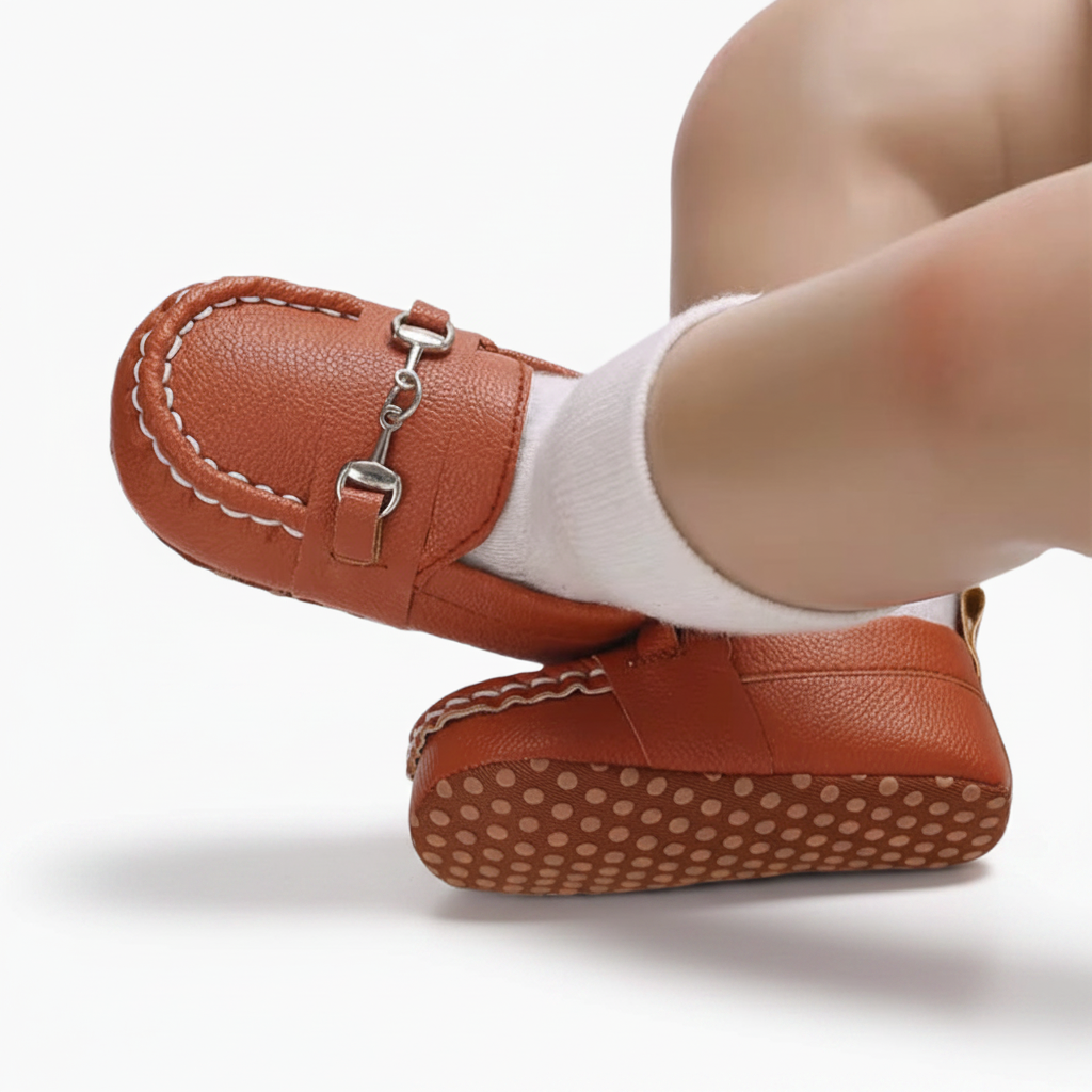 Pied de bébé chaussé d'un adorable mocassin marron à chaînette, symbole de douceur et d'élégance précoce.
