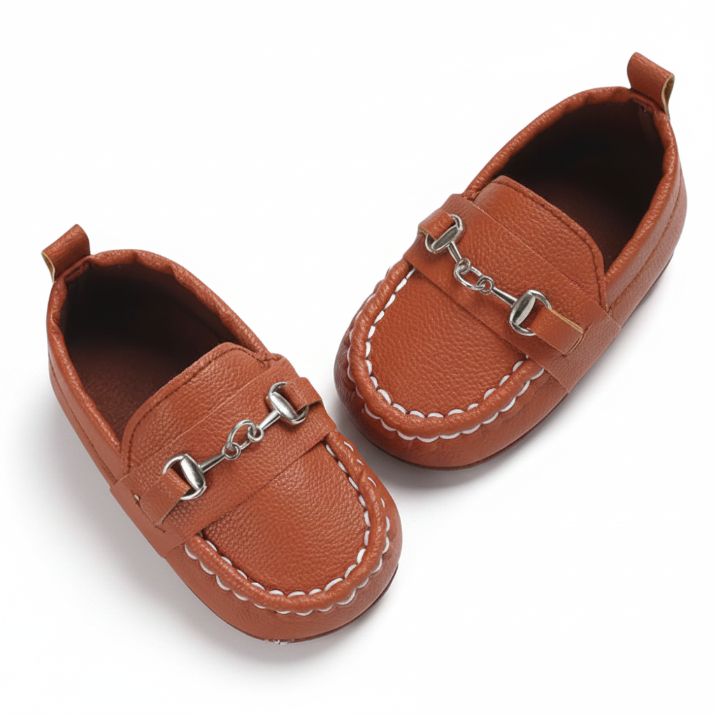 Paire de mocassins bébés marron à chaînette, élégamment posés sur un fond clair, mettant en valeur leur design intemporel.