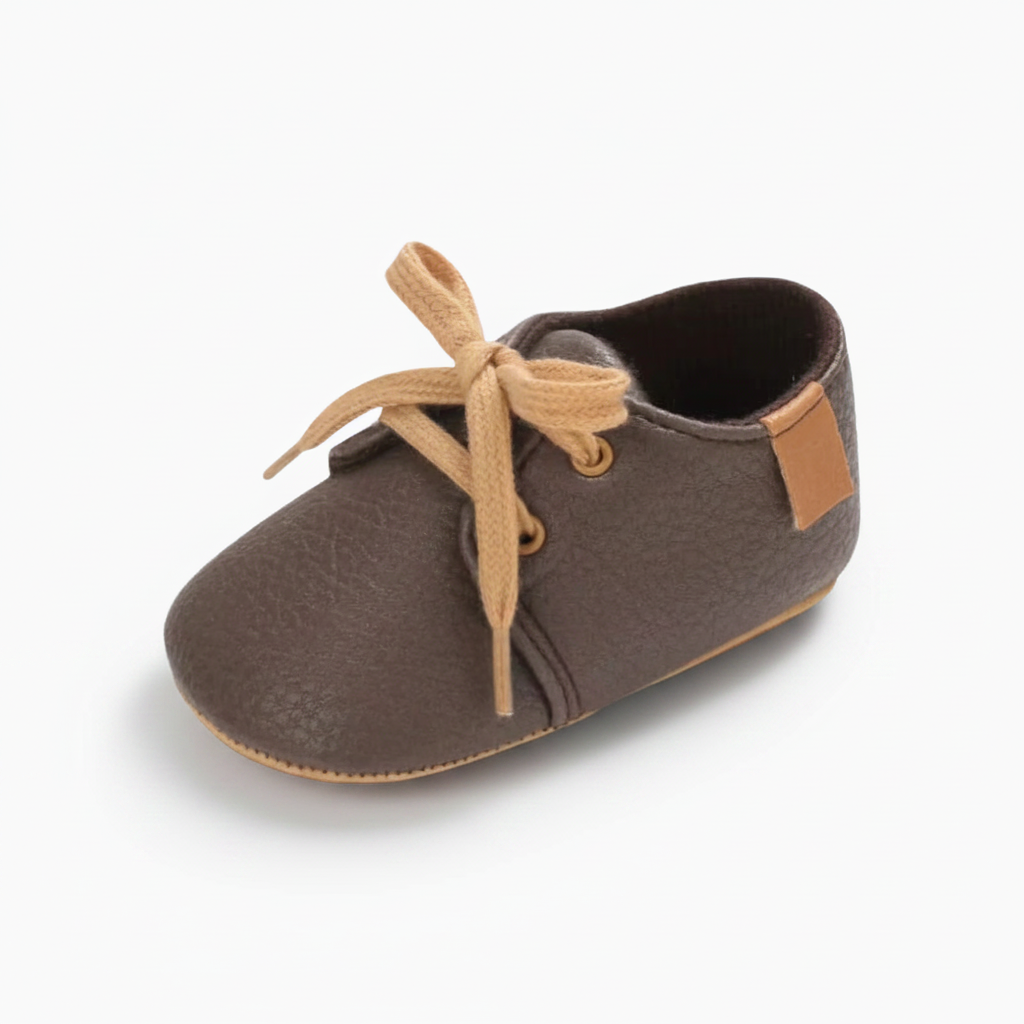 Mocassins bébé en cuir marron foncé, lacets ajustables, posés pour montrer l'élégance classique.