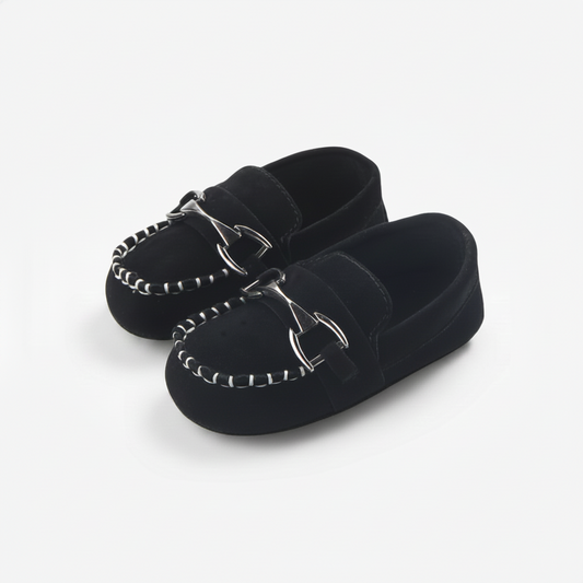 Premiers pas d'un enfant avec des mocassins noirs à chaînette, offrant style et soutien.