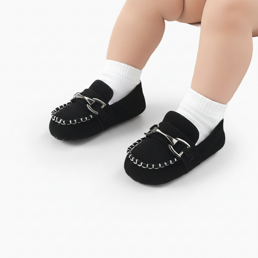 Gros plan sur la chaînette dorée ornant le dessus du mocassin bébé noir en cuir souple.