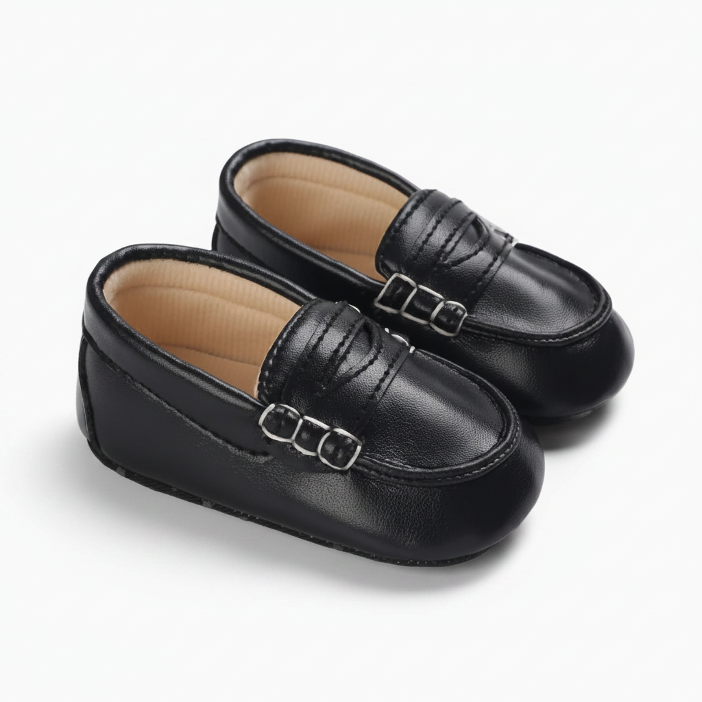Bébé souriant et jouant, ses adorables mocassins noirs complétant son look rétro chic.