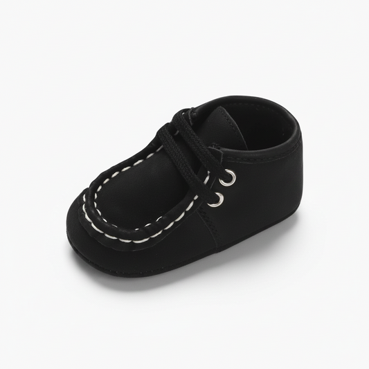 Mocassin bébé noir en daim avec détails blancs, idéal pour les premiers pas élégants.