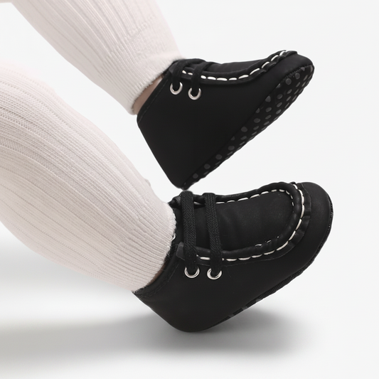 Gros plan sur le fini daim doux du mocassin bébé noir et ses subtils accents en tissu blanc.