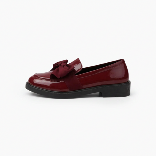 Pied portant un mocassin bordeaux vernis, en mouvement, reflétant la lumière avec sophistication.