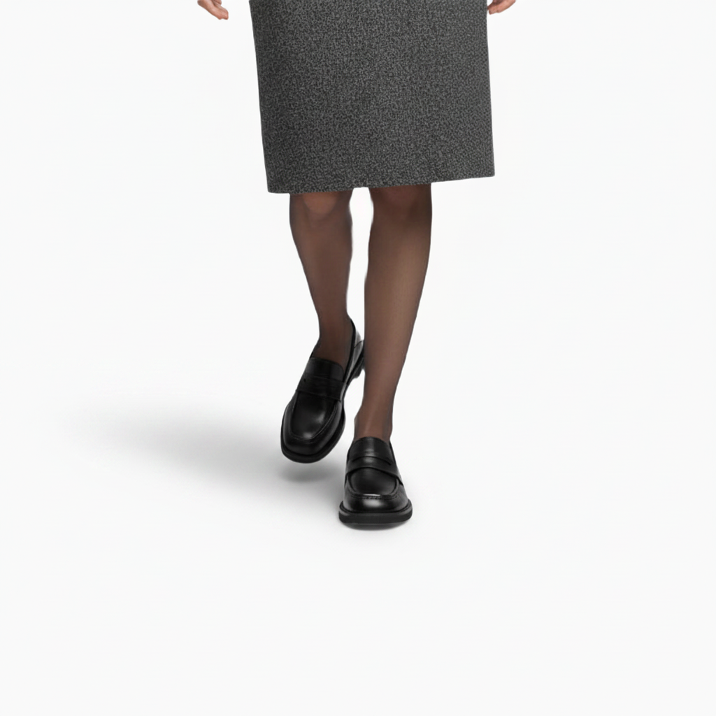 Mocassins à talon noir vernis assortis à un pantalon de tailleur, soulignant une tenue professionnelle chic.