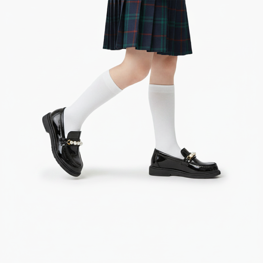 Paire de mocassins noirs pour enfant, posés délicatement, soulignant le lustre du cuir verni.
