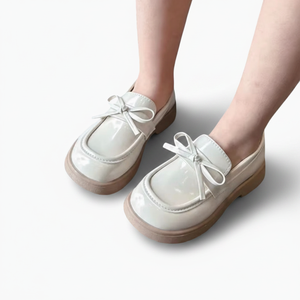 Gros plan sur le vernis éclatant du mocassin fillette beige, reflet subtil de la lumière.